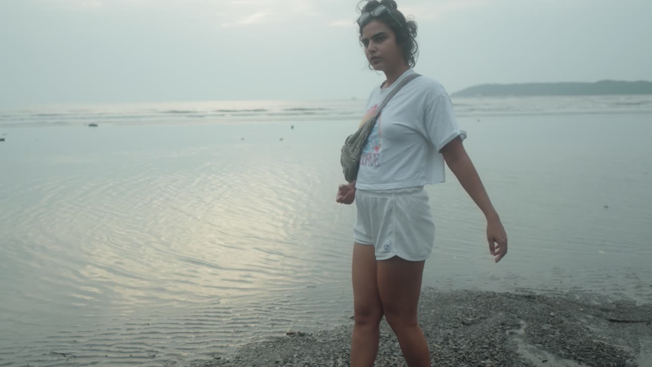 Giovane ragazza indiana cammina con grazia in mare su una spiaggia tropicale con un vestito bianco
