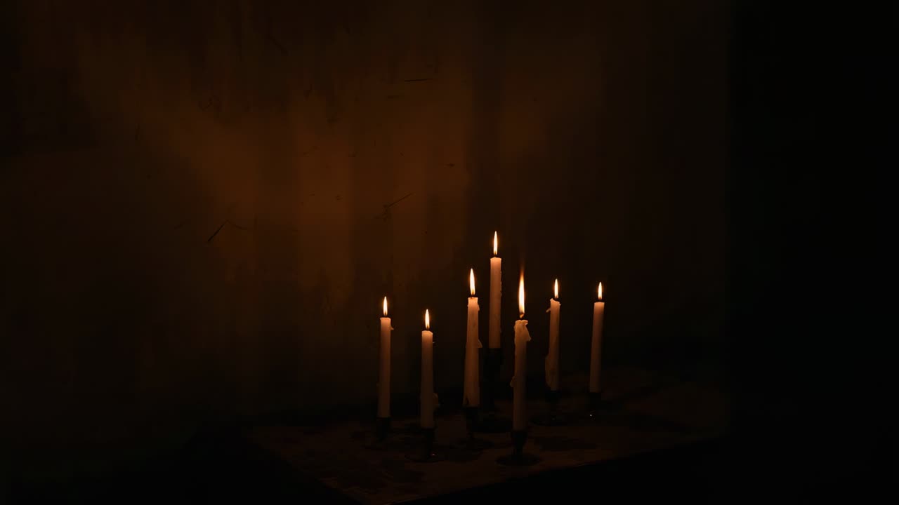Flickering nine white taper candles reacting to breeze on tabletop with melting wax, copy space