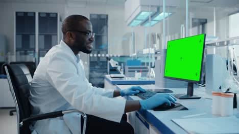 Modern Medical Research Laboratory: Scientist working on Computer Showing Green Chroma Key Screen. Scientific Lab, Medicine Development Facility with Advanced Equipment, Biotechnology. Side View Shot