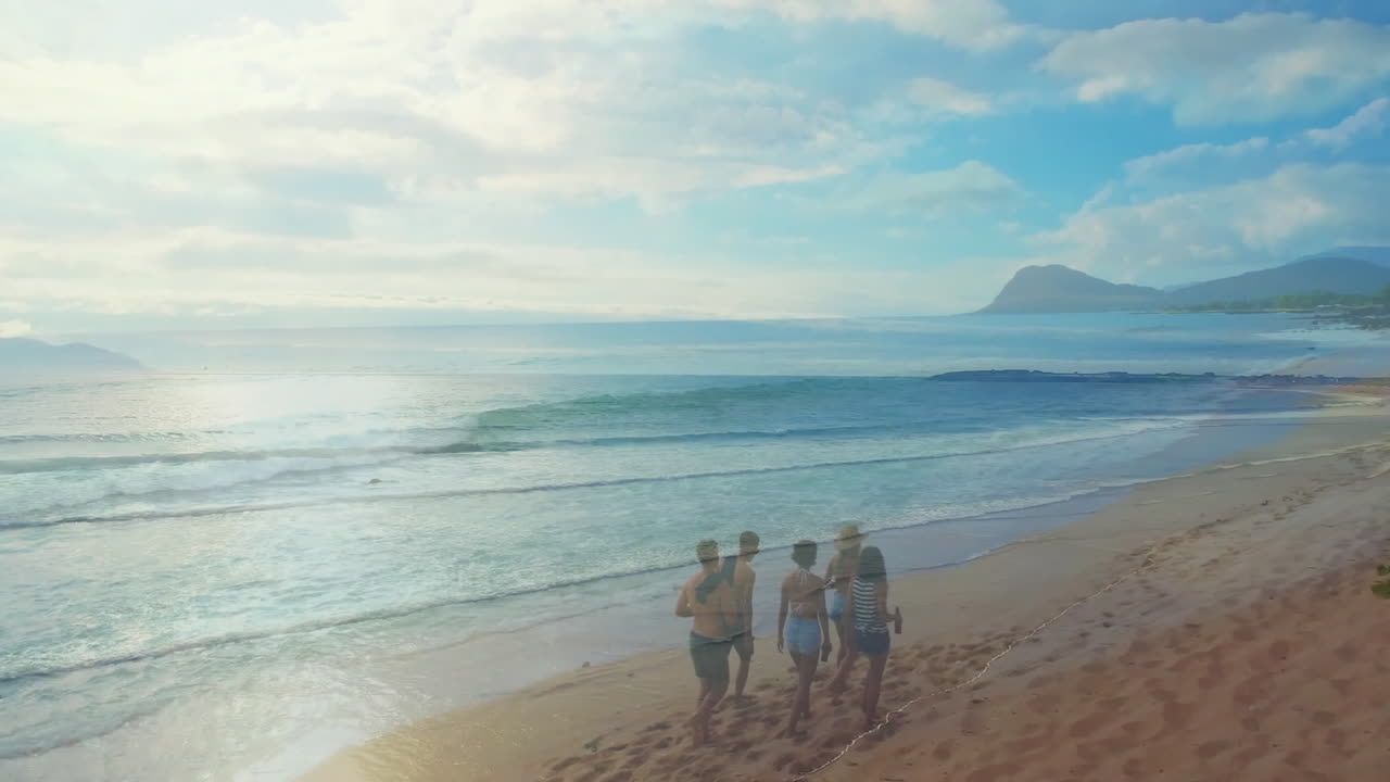 Walking along sandy beach, group enjoying ocean waves with distant mountains