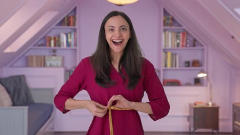 happy indian woman measuring her waist using inch tape