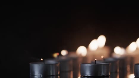 Video-of-close-up-of-rows-of-tea-candles-with-white-flames-and-copy-space-on-black-background