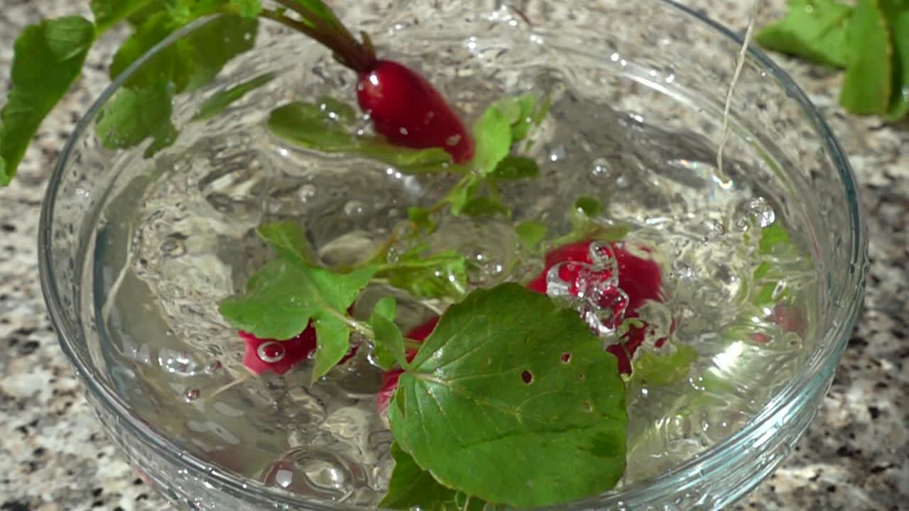 Caduta di ravanelli in una ciotola con acqua. Movimento rallentato.