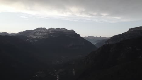 this drone video showcases a stunning frontal descriptive shot over the hecho valley in the aragonese pyrenees, spain, with snowy mountains in the background under a cloudy sunset sky.