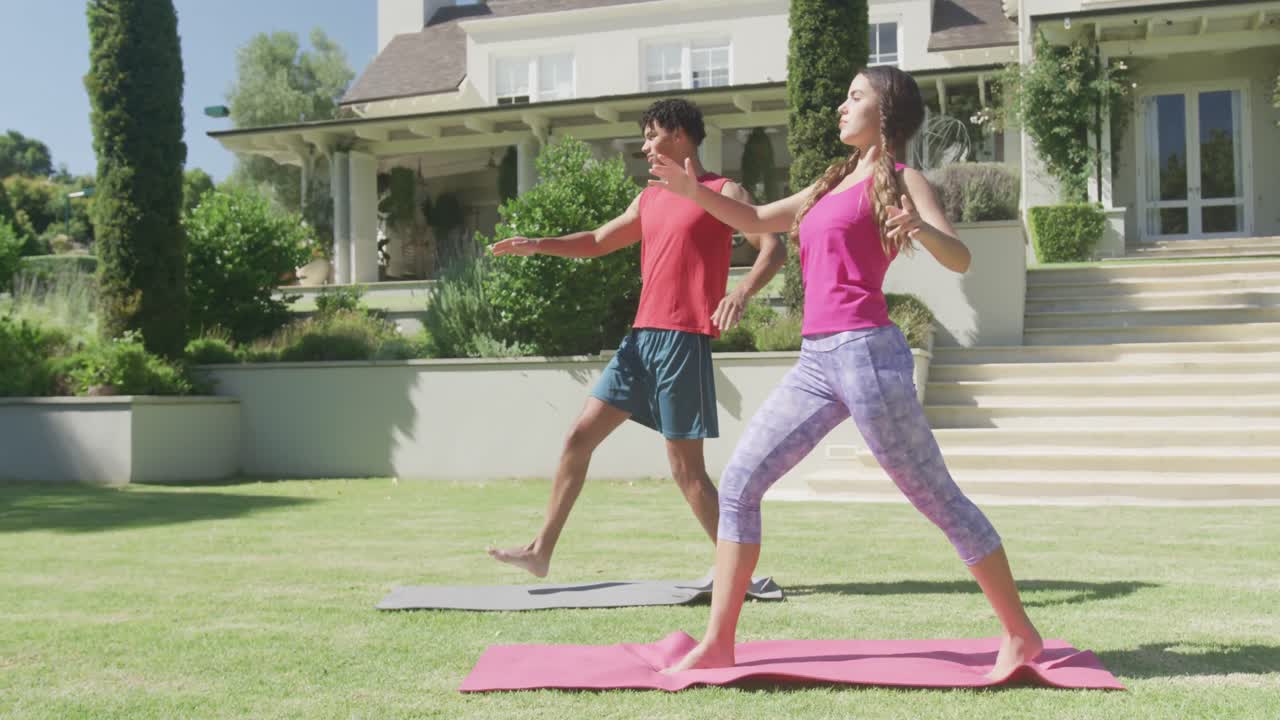 pareja biracial enfocada practicando yoga y haciendo poses en el jardín en un día soleado