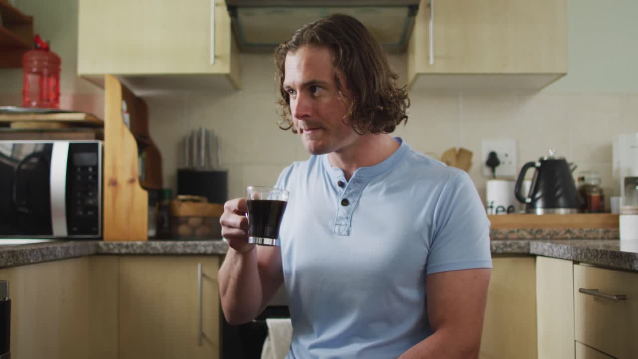 Happy caucasian disabled man in wheelchair drinking coffee in kitchen
