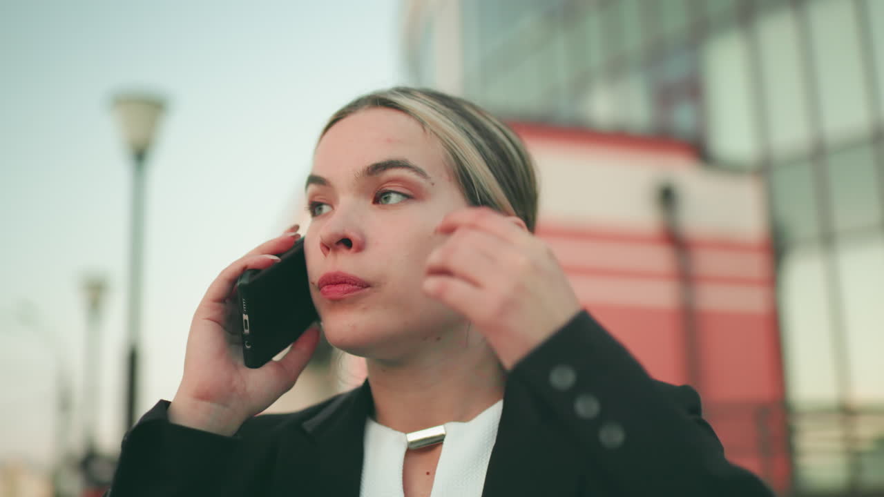 Angry lady in professional outfit on phone call looking exhausted and upset with slightly blurred building and two lampstands in background