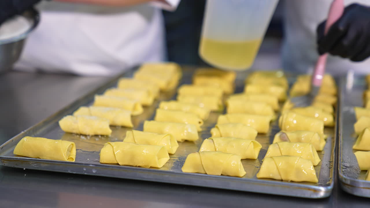 Little croissants are coated with egg and sugar. Sweet desserts are prepared for baking in the oven. Close up.