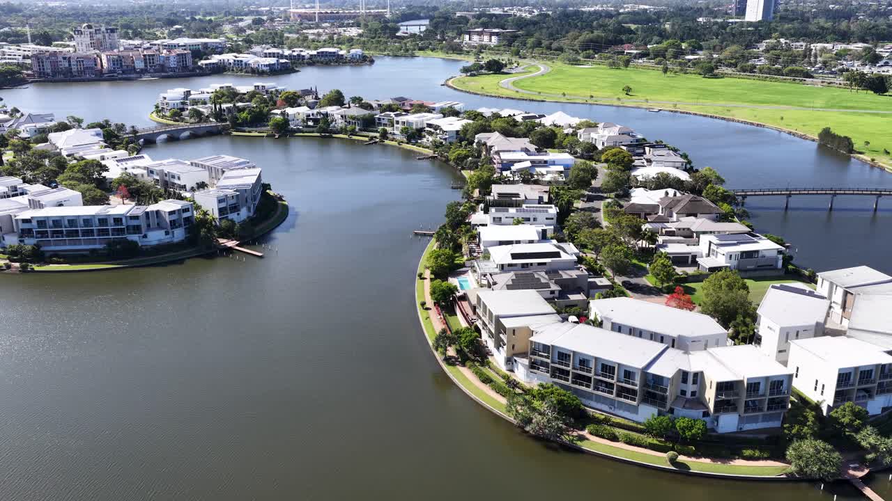 Aerial drone flyover of modern waterfront homes on curved lakeside peninsula under bright daylight
