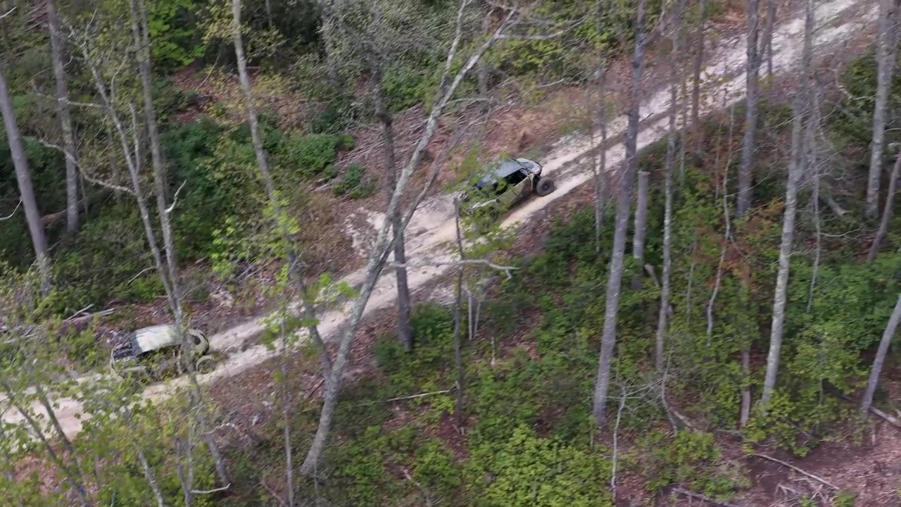 Riprese aeree con drone che seguono due veicoli ATV e UTV 4x4 affiancati per fuoristrada che guidano attraverso la foresta su un sentiero sterrato su per una collina insieme in gruppo