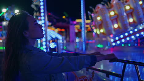 Amazed girl watching funfair carousel closeup. Dreamy young woman resting neon