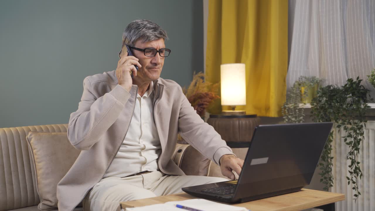 Gammel mand bruger bærbar computer og taler nervøst i telefon.
