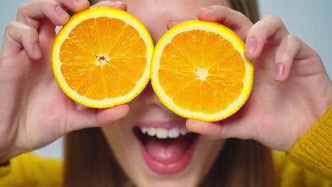 closeup young pretty woman making faces with two orange slices indoors.