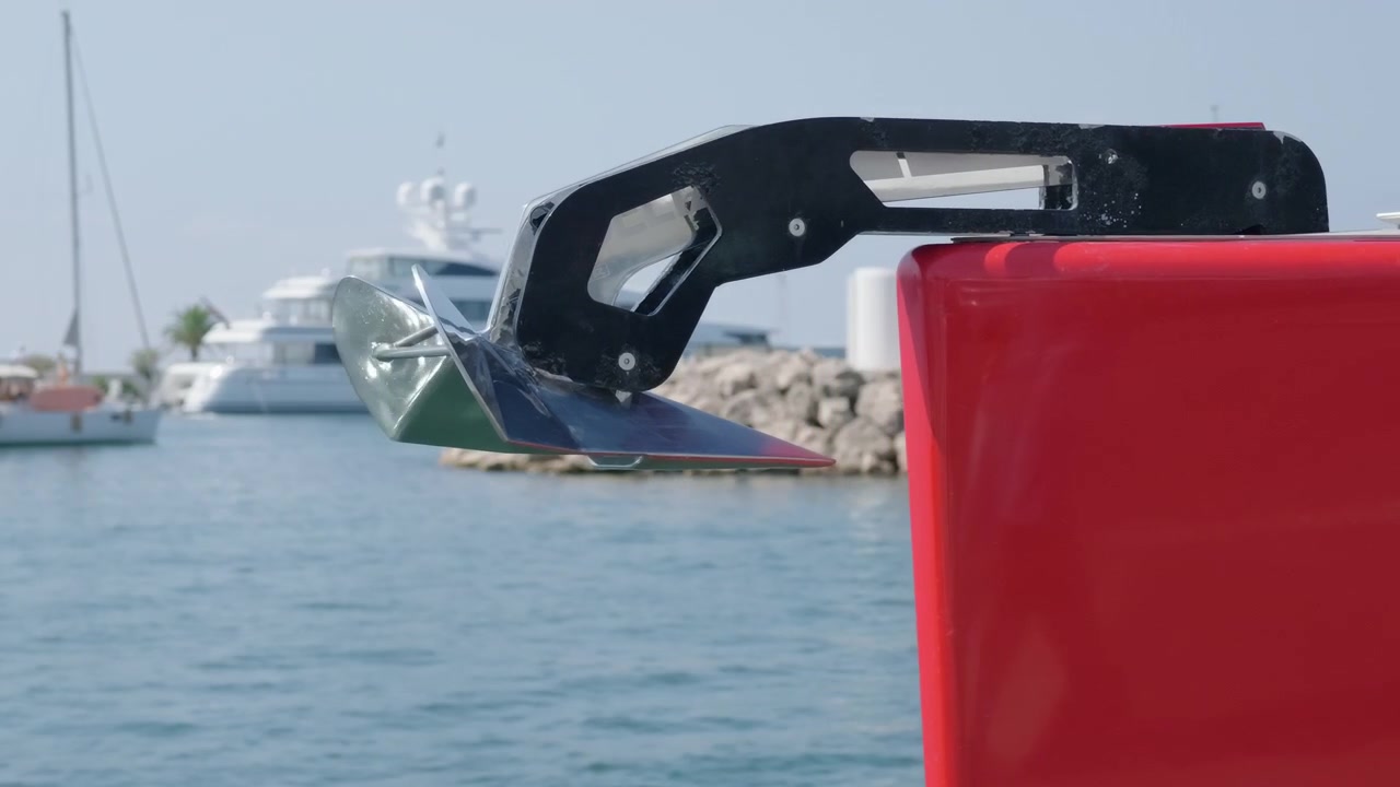 Nærbillede af et bådanker og rødt skrog nær en stenbølgebryder med fortøjede yachter, Côte d'Azur, Frankrig