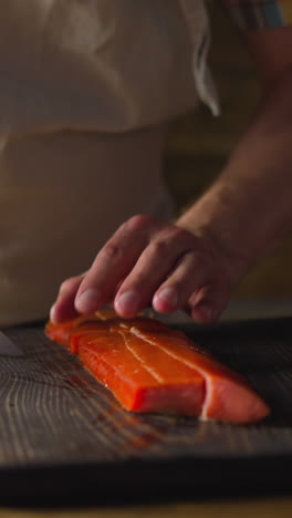 employee in apron cuts delicious cool smoked chum salmon fillet into pieces with knife on wooden board at countertop closeup slow motion. cooking seafood