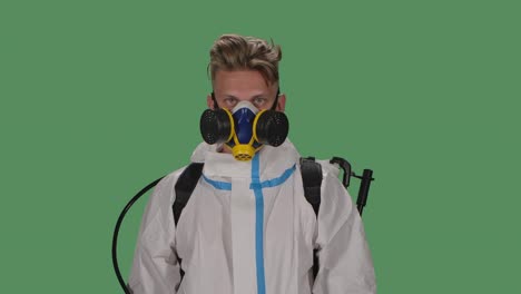 portrait young male in a protective suit, safety glasses, gloves and a respirator with a high pressure disinfectant looks confidently into the camera. green screen, chroma key. slow motion. close up