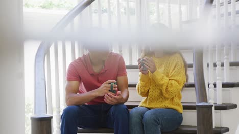 happy biracial couple spending time at home drinking coffee and sitting on stairs