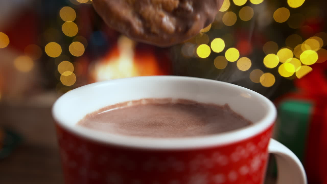 Mojando una galleta con chispas de chocolate en cacao en una taza roja, relajación navideña junto a la chimenea.