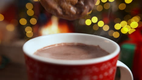 soaking a chocolate chip cookie in cocoa in a red mug, christmas relax by the fireplace
