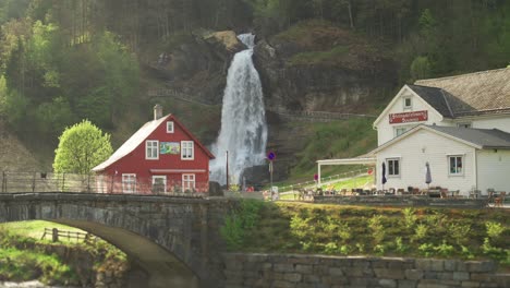 a famous steinsdalsfossen waterfall in the village of steine, norway.  the wall of whitewater falling off the mountain, water spray in hanging in the air. a small cafe is nearby, welcoming tourists