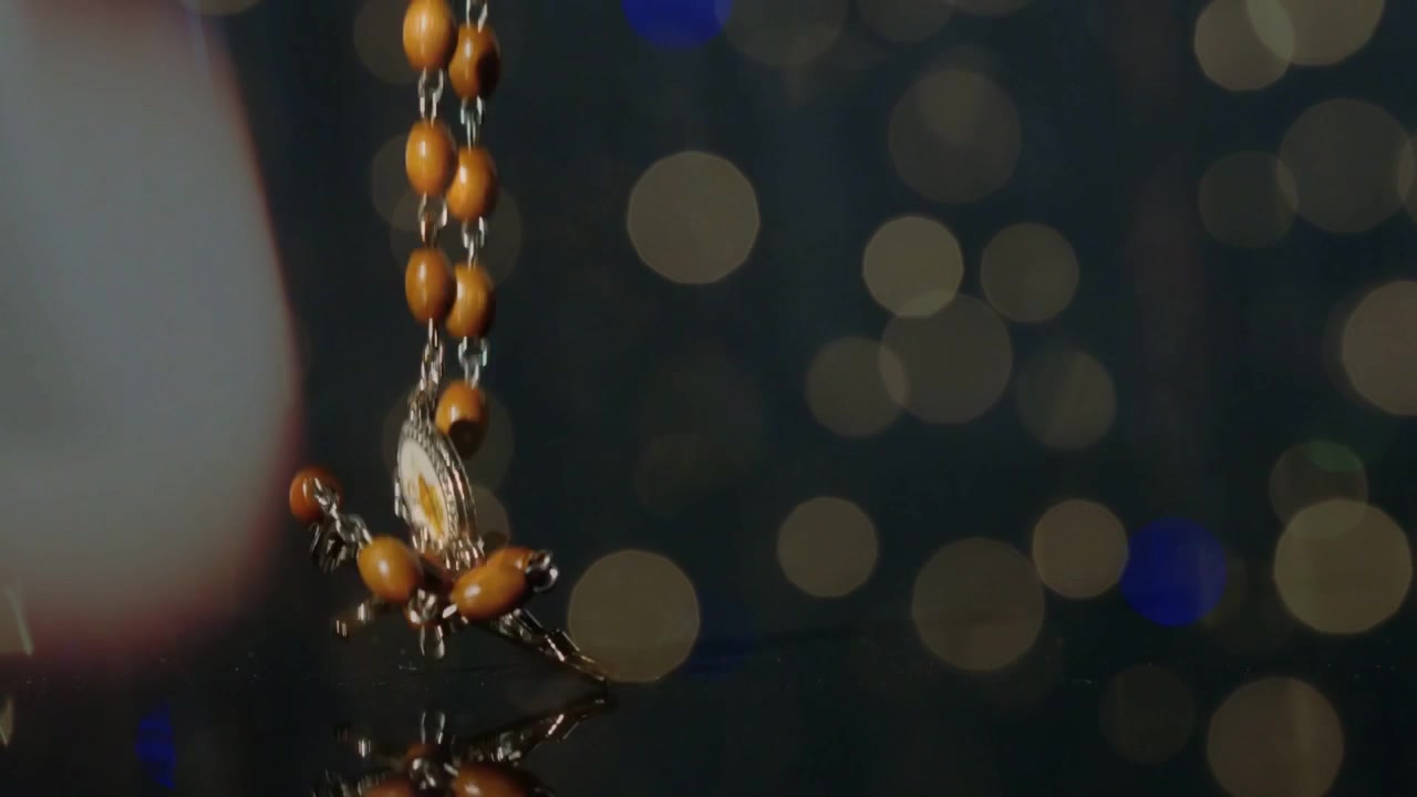 Rosary strand released from above, descending on glossy surface, beads tumbling forming mirror pile