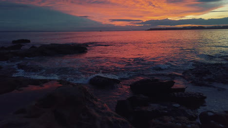 small waves crashing on australian coast during vivid sunset with burning clouds