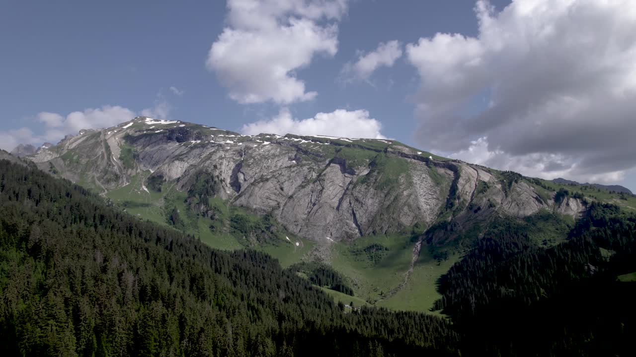 Aerial dynamic French Alps pine tree landscape with clouds in blue sky above mountain rocks at Lac du Mines d'Or [translation: Lake of Gold Mines] Tour de France vacation outdoor sports during summer