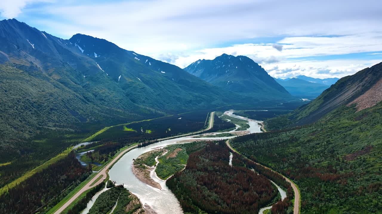 Branching river flowing in the green valley among the verdant mountains. Road goes along the river in Alaska, USA. Aerial view