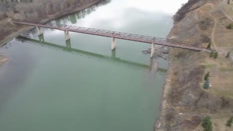 2-3-aerial-panaramic-twist-over-river-empty-park-by-a-truss-pedestrian-multimaterial-bridge-of-concrete-wood-and-steel-on-a-fall-afternoon-where-merky-poluted-waters-appear-by-a-beavers-home-fall-day