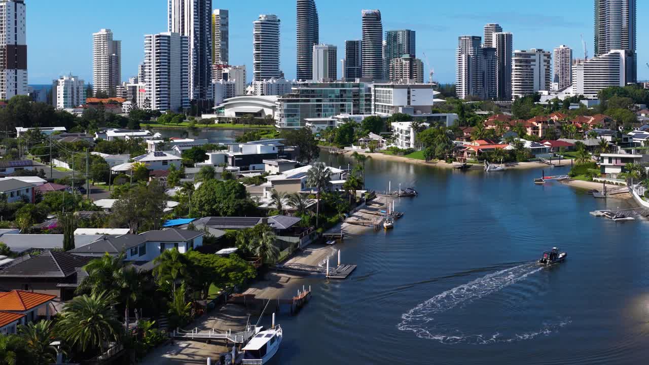 A boat navigates a scenic waterway with city skyline in the background, under bright daylight on the Gold Coast, Australia