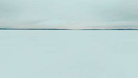 flying over a road on frozen lake ice to reveal a snowy forest in the horizon