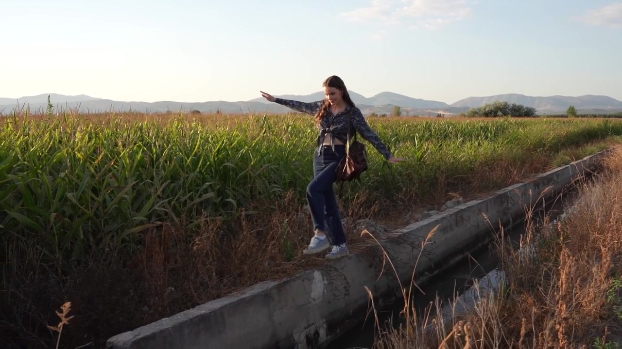 Uma jovem que está de pé em um caminho de concreto ao lado de belos campos verdes