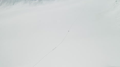 panorama a ojo de pájaro, los alpinistas se mueven en un amplio campo de nieve, ascienden a la cima de una montaña
