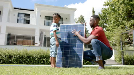 padre y hijo afroamericanos examinan un panel solar al aire libre en casa