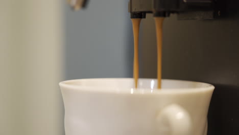 The-coffee-machine-prepares-a-coffee-drink,-two-thin-streams-pour-into-a-white-mug