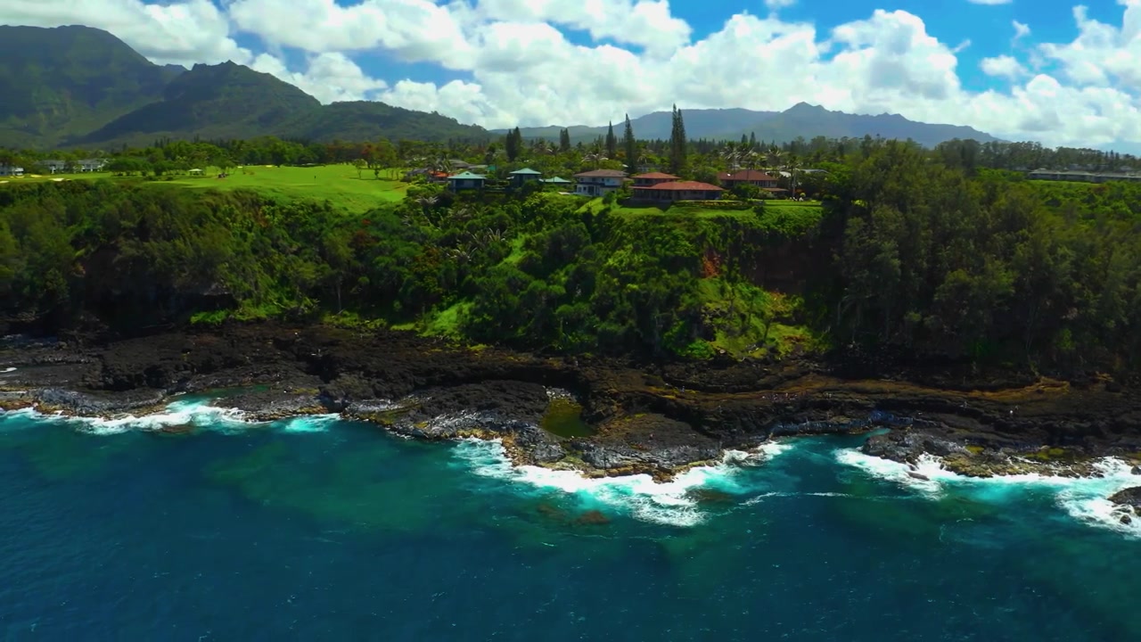 Un panorama aereo cinematografico mozzafiato con ripresa aerea che scivola con grazia su aspre scogliere marine di lava nera, acque turchesi incontaminate e lussureggianti tenute costiere color smeraldo sulla leggendaria costa nord di Kauai