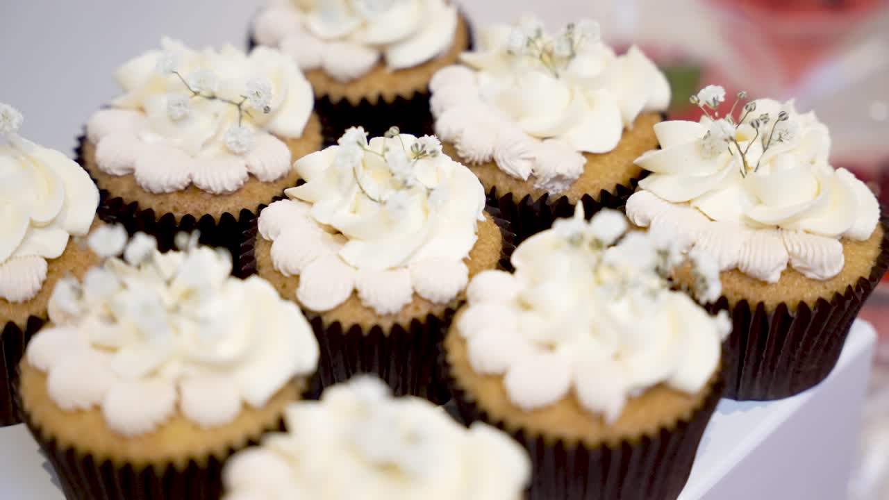 Una fila di cupcake alla vaniglia con glassa di panna fresca e piccoli fiori bianchi in esposizione. Queste dolci delizie sono perfette per un dessert di matrimonio o una festa di compleanno