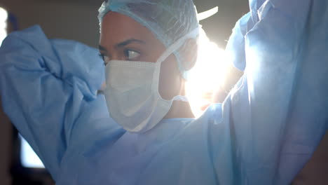 biracial female surgeon wearing face mask in operating theatre, slow motion