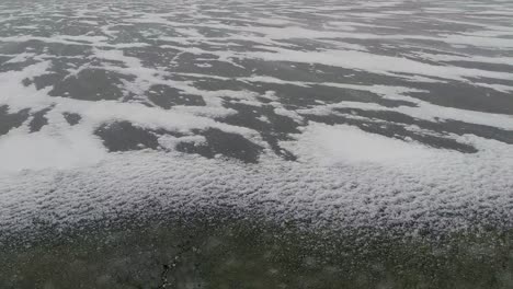 slow pan up of cold blowing snow accumulating along cracks in ice as the water freezes