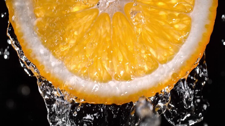 rodaja de naranja y salpicaduras de agua en el fondo negro en cámara lenta