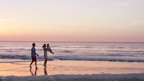 happy family on the beach holding hands swinging little girl around at sunset on vacation