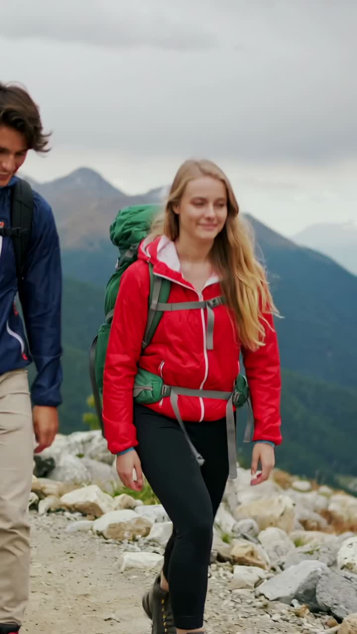 Video verticale: coppia che cammina e parla, percorrendo un sentiero roccioso, con giubbotti rossi e blu e uno zaino verde