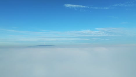 aerial video: drone flies backward, revealing a lone skyscraper amidst thick clouds on the left