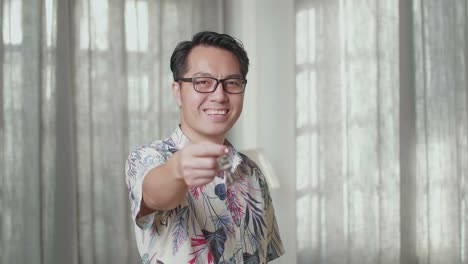 카드보드 상자를 가진 아시아 남자의 클로즈업 미소와 새로운 집에서 카메라에 열를 보여