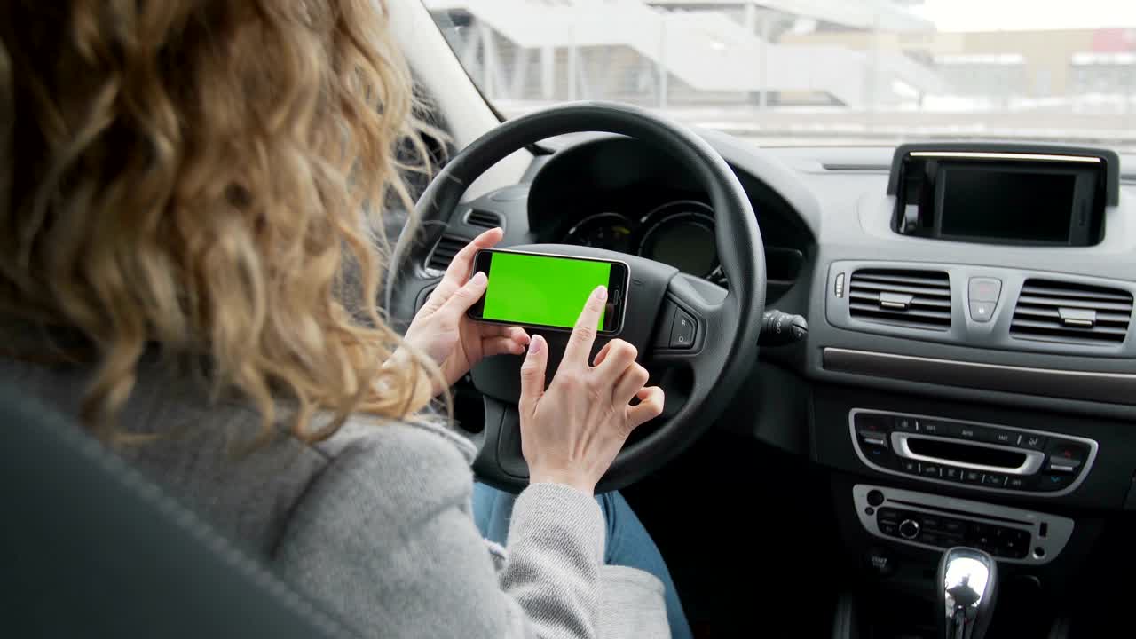 mujer se sienta en el coche moderno y trabaja en el teléfono inteligente - pantalla verde - primer plano