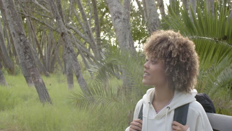 young biracial woman with curly hair smiles in a forest setting with copy space