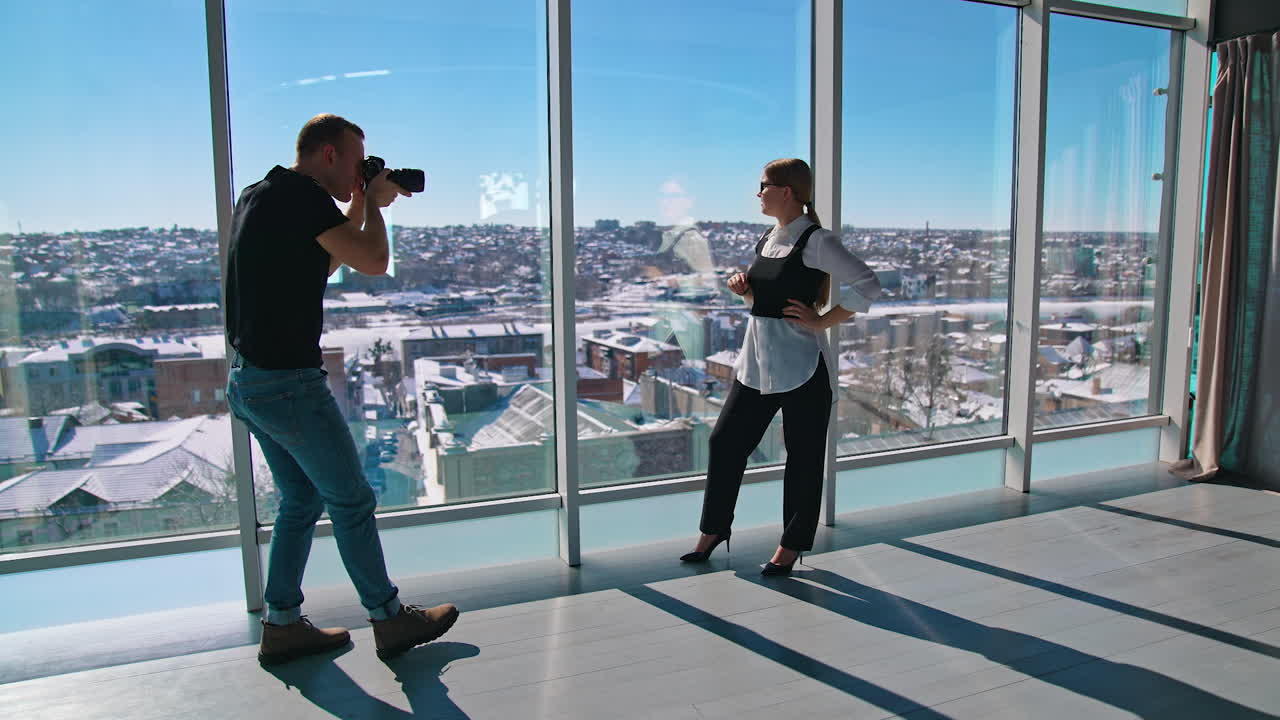 Attractive business woman poses to a photographer. Young female in glasses in black and white clothes posing on camera near large window indoors.