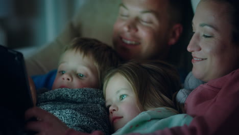 happy family using tablet computer with children mother and father enjoying watching entertainment with kids on touchscreen technology relaxing before bedtime