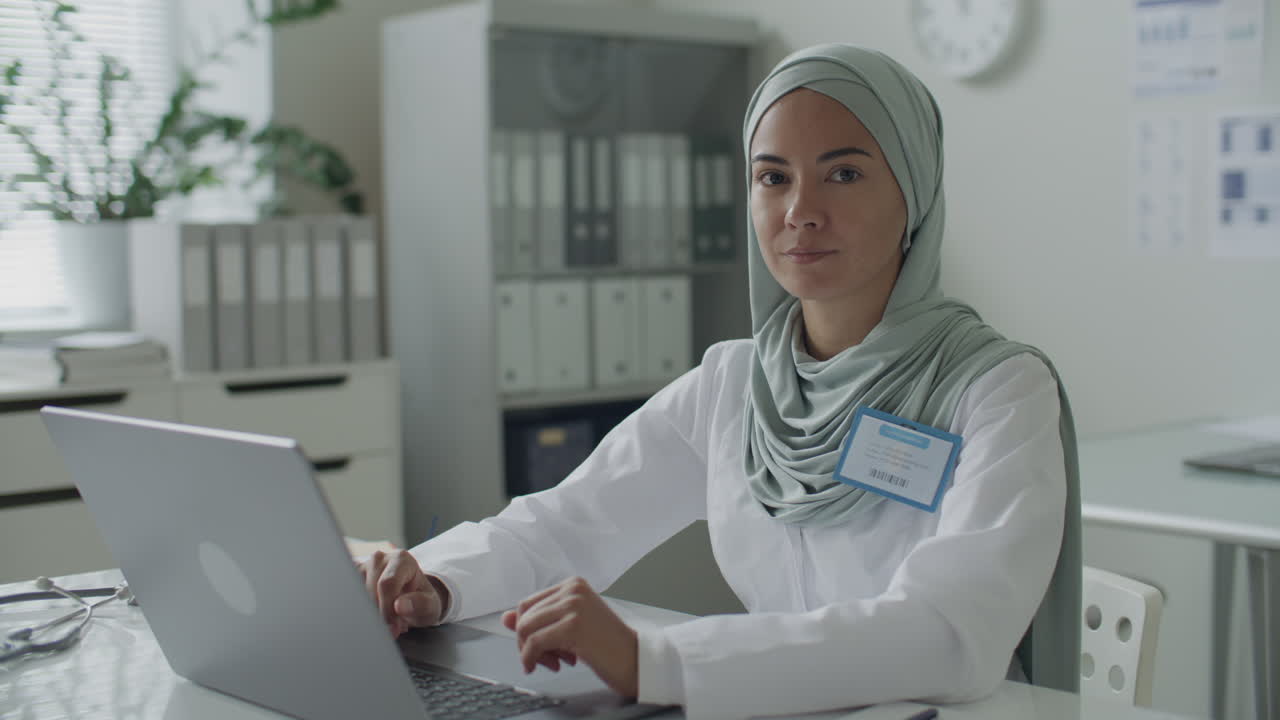 Portrait of Beautiful Female Doctor in Hijab Working on Laptop in Medical Office