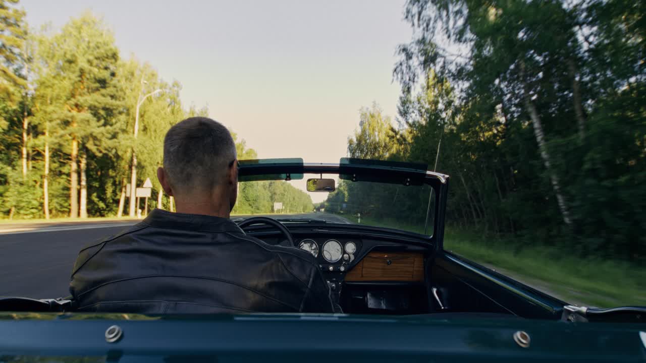 Mann fährt ein Cabrio auf einer von Bäumen gesäumten Straße